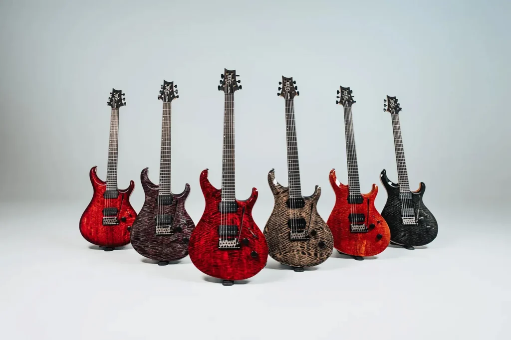Colección de guitarras eléctricas de la gama PRS Tekton T, mostrando seis modelos con tapas de arce figurado en acabados rojo, morado, natural, naranja y negro, equipados con configuración de doble humbucker, puente de trémolo y diseño de doble cutaway desarrollado para un enfoque moderno y de altas prestaciones.