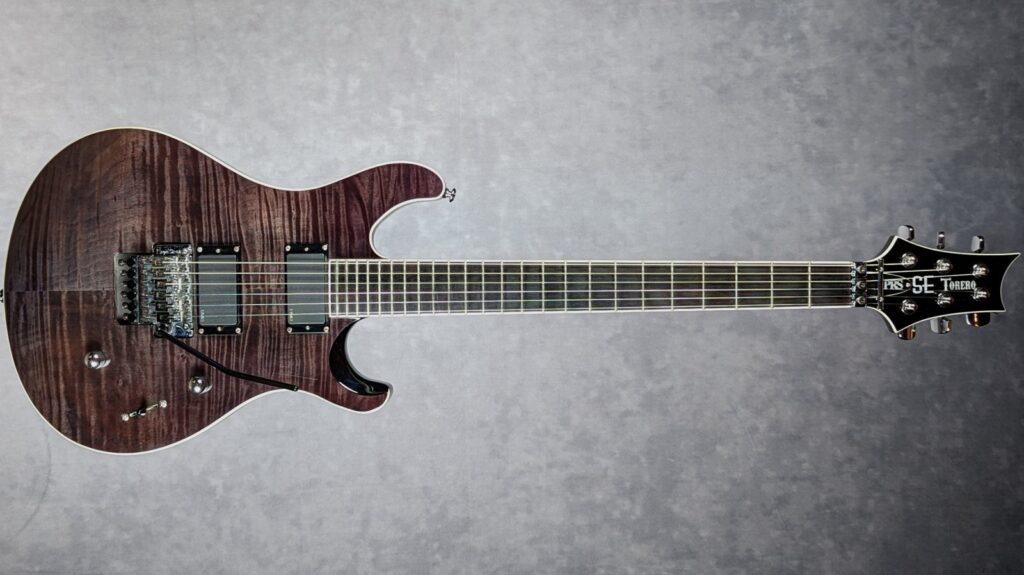 PRS Tekton: análisis de la nueva gama de PRS para el guitarrista técnico y moderno 7 PRS SE Torero con acabado translúcido oscuro sobre tapa de arce flameado, equipada con dos pastillas activas EMG, puente Floyd Rose con sistema de doble bloqueo, diapasón de ébano de 24 trastes y clavijero PRS SE Torero, mostrada en vista frontal sobre fondo gris.
